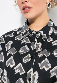 Camicia nera con bottoni, caratterizzata da un motivo astratto a contrasto in grigio e bianco, con colletto a punta e una texture di tessuto liscia.