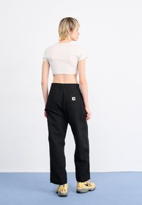T-shirt beige coupé et pantalon cargo noir taille haute avec des détails de poches. Le modèle porte des chaussures jaunes avec une semelle texturée.