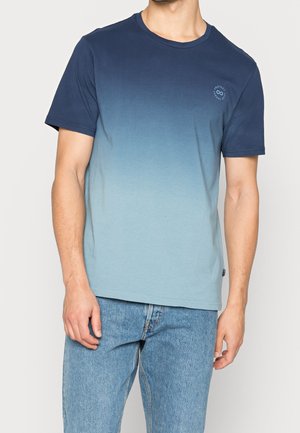 Mann trägt ein kurzärmeliges Ombre-T-Shirt, das von Marineblau zu Hellblau verläuft, kombiniert mit blauen Jeans.