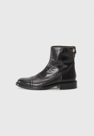Bottine en cuir noir avec bout rond, couture décorative et petit bouton accent. Présente un petit talon empilé. Texture lisse.