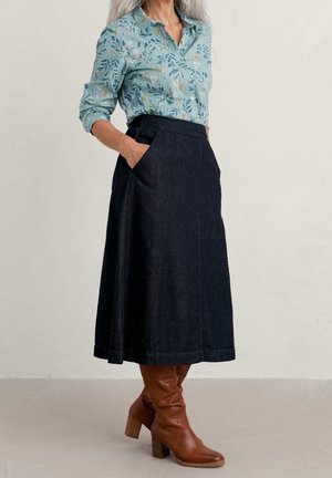 Jeansskørt med sidelommer, mørkeblå farve, svajet design. Samparet med en lyseblå skjorte med blomsterprint og brune knæhøje støvler.