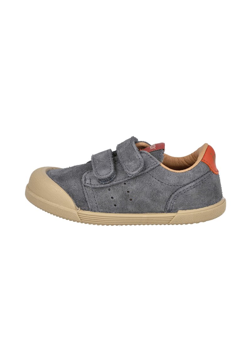 Zapato de ante gris con dos correas de velcro, punta redondeada, suela de goma crema, pequeños orificios de ventilación y un acento rojo en el talón.