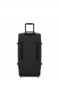 La valise noire à roulettes est dotée d'un extérieur en tissu résistant, d'une poignée télescopique, de quatre roues et de sangles sécurisées sur les côtés.