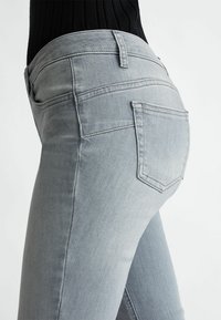 Jeans in denim grigio chiaro con vestibilità slim, caratterizzati da un design a cinque tasche e cuciture sottili. La cintura ha una finitura liscia con hardware minimale.