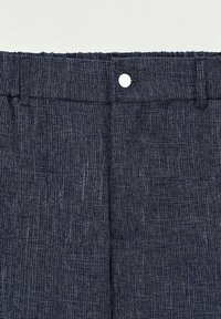 Gros plan sur un tissu texturé bleu foncé, avec une ceinture, un bouton blanc et des motifs tissés subtils.