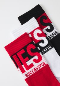 Tre paia di calzini nei colori rosso, bianco e nero, caratterizzati da una texture a coste e con la scritta "SUCCESSFUL" in colori a contrasto.