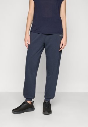 Marineblå joggebukser med avsmalnende mansjetter og elastisk midjebånd, kombinert med en marineblå t-skjorte med kort erme og svarte joggesko.