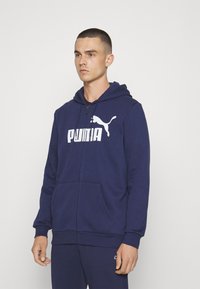 Námořnická mikina na zip vyrobená z měkké tkaniny. Disponuje velkým bílým logem "PUMA" na hrudi a klokaními kapsami. Součástí je kapuce se stahovací šňůrkou.