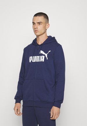 Felpa con zip color navy realizzata in tessuto morbido. Presenta un grande logo bianco "PUMA" sul petto e tasche a marsupio. Cappuccio con cordini incluso.