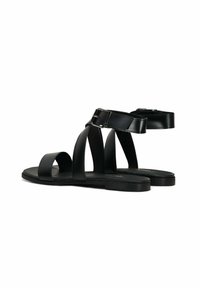 Sandali in pelle nera con suola piatta, caratterizzati da molteplici cinturini incrociati e una fibbia regolabile alla caviglia per il supporto. Texture liscia.