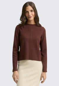 Pull maroon à manches longues et col rond, avec un détail de couture au centre devant. Porté sur une jupe beige clair.