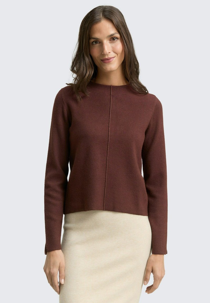 Pull maroon à manches longues et col rond, avec un détail de couture au centre devant. Porté sur une jupe beige clair.