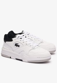 Zapatillas de cuero blancas con un collar texturizado en negro y gris. Cuentan con cordones blancos, punta perforada y un detalle negro en la suela.