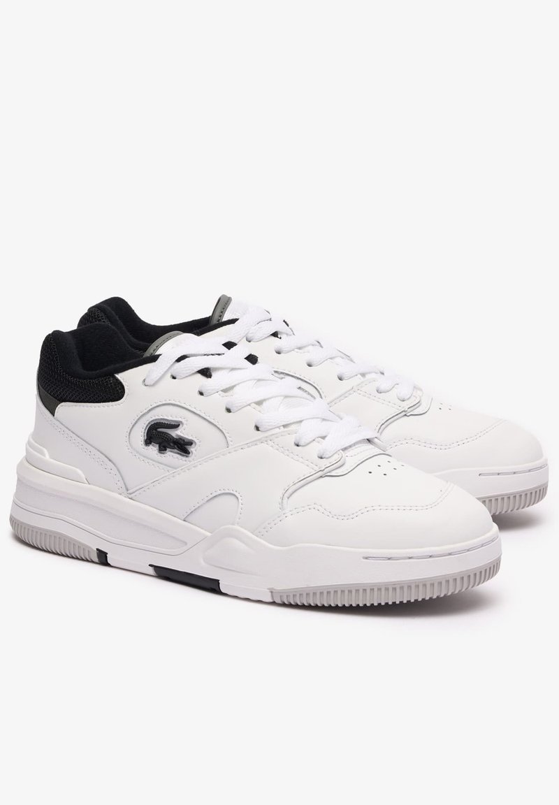 Baskets en cuir blanc avec un col texturé noir et gris. Elles présentent des lacets blancs, une pointe perforée et un accent noir sur la semelle.