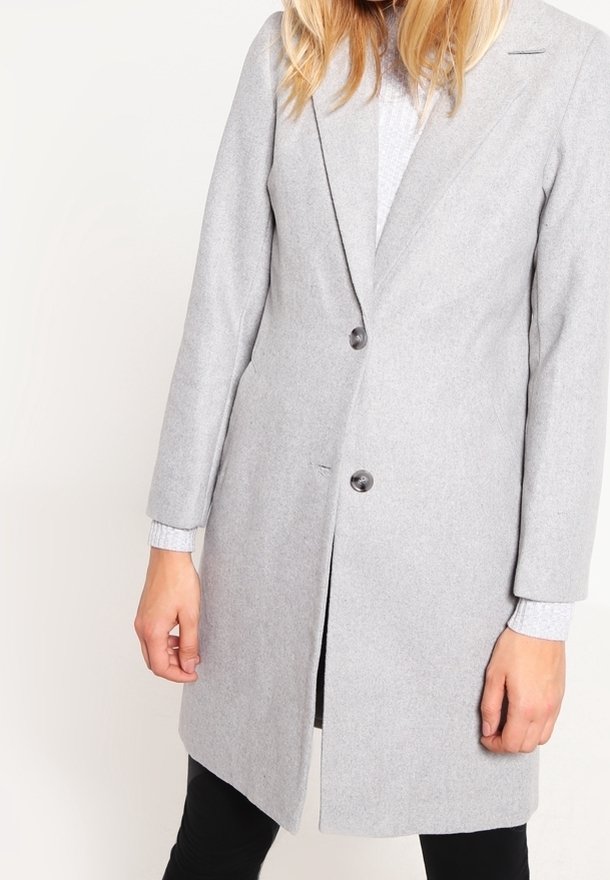 Kobieta nosząca jasnoszary, wełniany płaszcz do kolan z dwoma guzikami z przodu, na jasnoszarym swetrze.