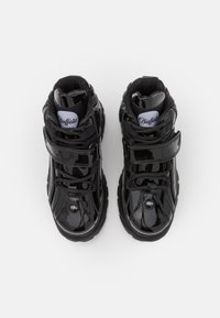 Black patent leather high-top sneakers with Velcro strap, padded collar, textured sole, and logo detail on tongue.