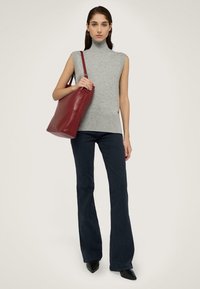Suéter gris sin mangas de cuello alto combinado con jeans acampanados de un azul oscuro; la modelo lleva un bolso tote de cuero rojo; zapatos negros de punta.
