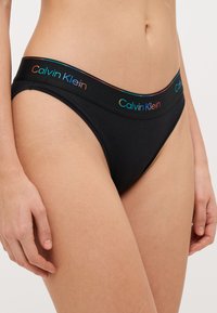Črne bombažne tangice z večbarvnim pasom Calvin Klein, gladka tekstura in minimalističen dizajn.