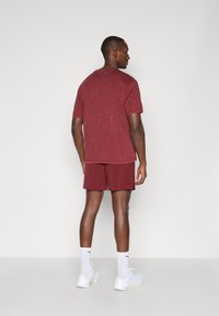 Bordeaux sport T-shirt met korte mouwen en een ronde hals, gecombineerd met bijpassende shorts. Draagt met witte sokken en sneakers. Gladde textuur.