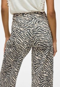 Beige leveled pants dengan pola zebra hitam, menampilkan dua kantong belakang dan desain pinggang tinggi. Terbuat dari kain lembut dan bertekstur.