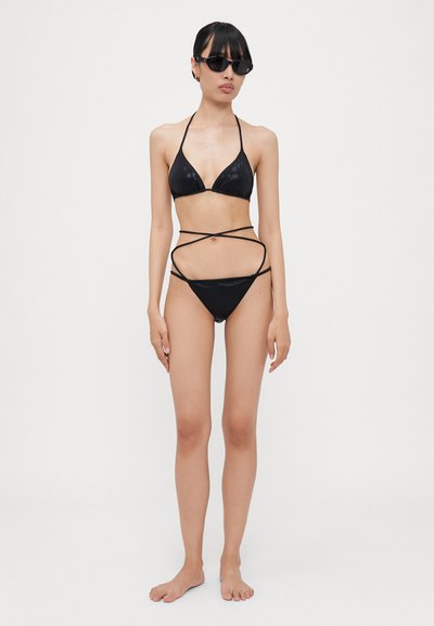 Črni bikini komplet, ki vključuje trikotni top in dno z izrezanimi detajli. Material ima sijoč zaključek in vsebuje tanke naramnice.