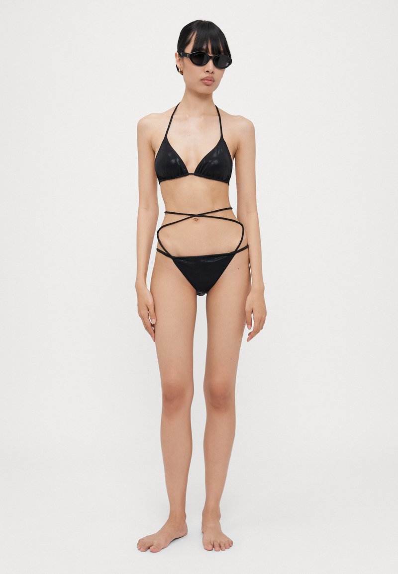 Black bikini set featuring a triangular top and bottom with cut-out detailing. The material has a glossy finish and includes thin straps.
