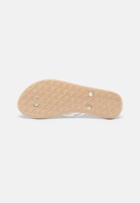 Semelle de chaussure en matériau caoutchouté brun clair, présentant un motif géométrique texturé et deux rivets circulaires pour une meilleure adhérence.