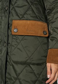 Veste matelassée vert olive avec rabat de poche en velours côtelé marron et poignets, arborant le logo Barbour et des boutons-pression noirs.