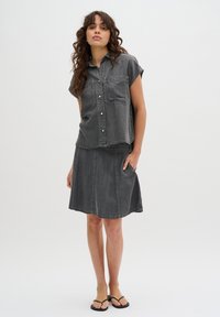 Camicia a maniche corte in denim grigio con due tasche frontali, abbinata a una gonna in denim coordinata. Entrambi i capi presentano cuciture a contrasto e un taglio rilassato.