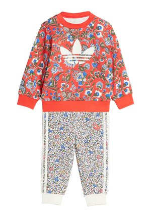 Sweat-shirt rouge à fleurs avec logo blanc, associé à un pantalon blanc à motif floral et bandes latérales. Les deux vêtements ont des poignets côtelés.