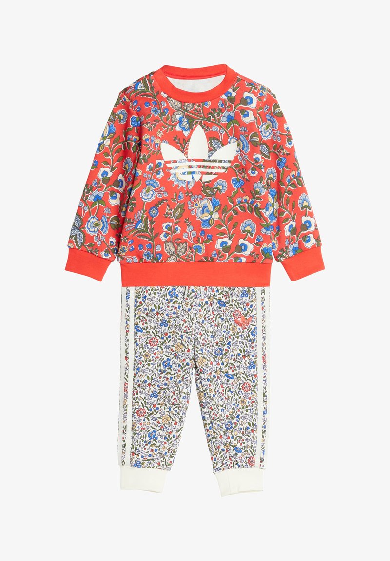 Sweat-shirt rouge à fleurs avec logo blanc, associé à un pantalon blanc à motif floral et bandes latérales. Les deux vêtements ont des poignets côtelés.