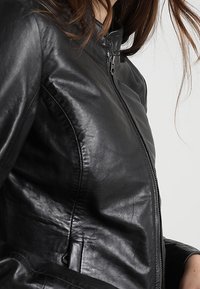 Černá kožená bunda s těsným střihem, vybavená vysokým límcem a zipovým zapínáním. Hladká textura a minimální detaily.