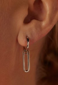 Zilveren oorbellen met een paperclip ontwerp, met een gepolijste afwerking, hangend aan een kleine hoop. Close-up van het oor.