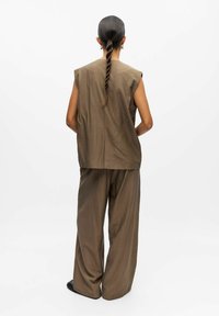 Top marrone senza maniche con schiena aperta e pantaloni marroni a gamba larga. Tessuto liscio con una leggera lucentezza, caratterizzato da un design minimalista e senza pattern.