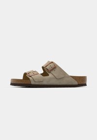Beige Wildleder-Sandalen mit zwei verstellbaren Riemen, ausgestattet mit Kupfer-Hardware-Akzenten und einem Korkfußbett für Komfort, auf einer strukturierten Laufsohle.