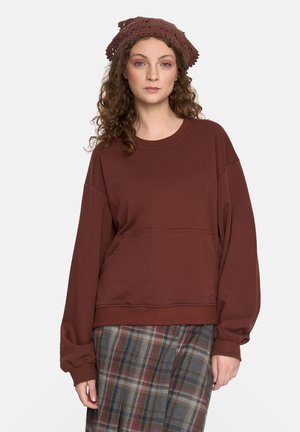 Brązowy sweatshirt z okrągłym dekoltem, luźny krój i długie rękawy. Posiada przednią kieszeń i jest zestawiony z spódnicą w kratę.