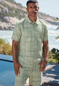 Lys grøn kortærmet polo shirt med et struktureret mønster. Har en krave og to knapper, parret med matchende shorts.