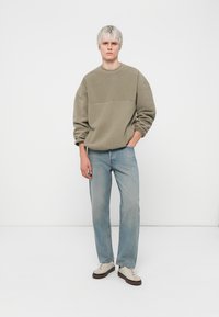 Lys olivengrønn oversized sweatshirt med rund hals, sammen med lyseblå rette jeans og beige sneakers.