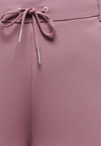 Meko, teksturirano platno u boji prljave ruže, s zatvaranjem na vezanje s metalnim vrhovima, integriranim pojasom i prošivenim šavovima.