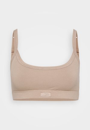 Küljelt ribitud beež rinnahoidja laia rihmaga ja pehme tekstuuriga. Omab logotagi rihmal, disainitud mugavuseks ja toetuseks.