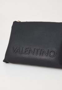 Clutch bag in pelle nera testurizzata con logo "VALENTINO" in rilievo. Presenta una chiusura con zip e dettagli lisci lungo i bordi.