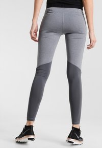Leggings sportivi grigi hanno un design aderente con un motivo a blocchi di colore che combina sezioni grigie chiare e scure, realizzati in tessuto elastico.