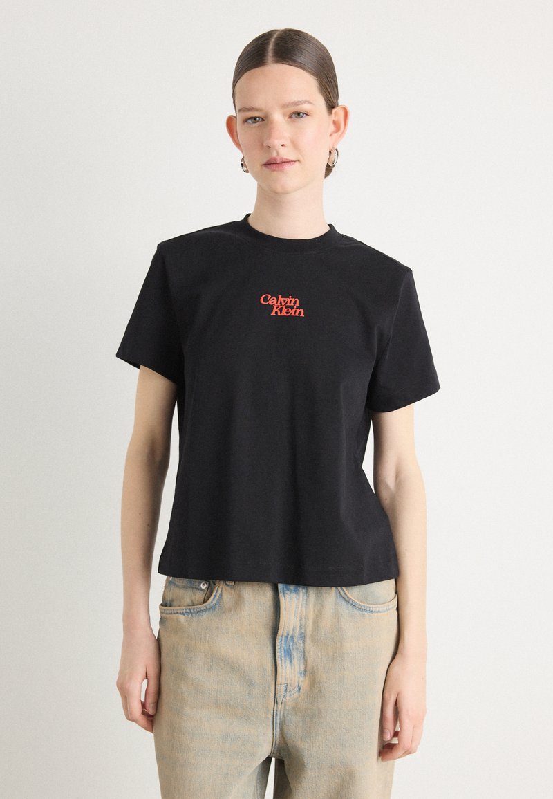 Svart bomullst-skjorte med rund hals og korte ermer, med en rød brodert "Calvin Klein" logo på forsiden.
