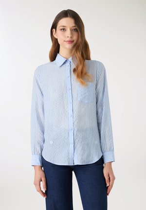Camicia a righe azzurro chiaro con bottoni, taschino sul petto, trama sottile e maniche lunghe. Il tessuto è semi-trasparente con una finitura liscia.