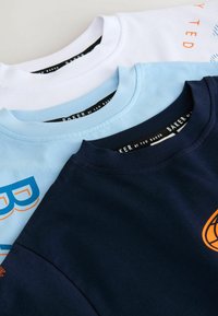 Kolm t-särki virnas: valge, helesinine ja tumesinine. Puuvillane materjal, ümara lõikega kaelused ja iga särgi ees nähtavad musta värvi kaubamärgi sildid.