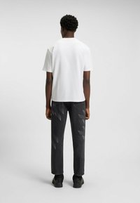 Weißes T-Shirt mit kurzen Ärmeln, kombiniert mit dunkelgrauen Jeans mit einem geometrischen Muster, von hinten gesehen, mit schwarzen Schuhen.