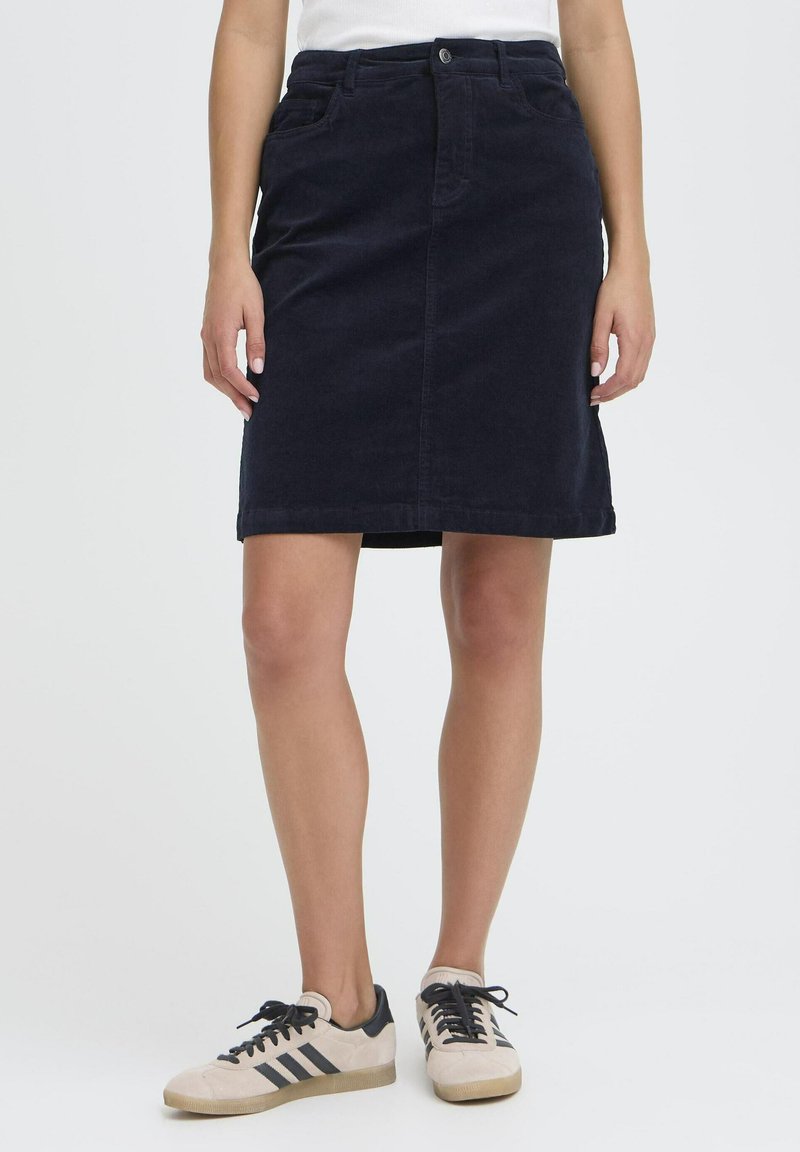 Temno modra kord skirt dolžine do kolen z sprednjim gumbom, zankami za pas in žepi, v kombinaciji s bež in črnimi supergami.