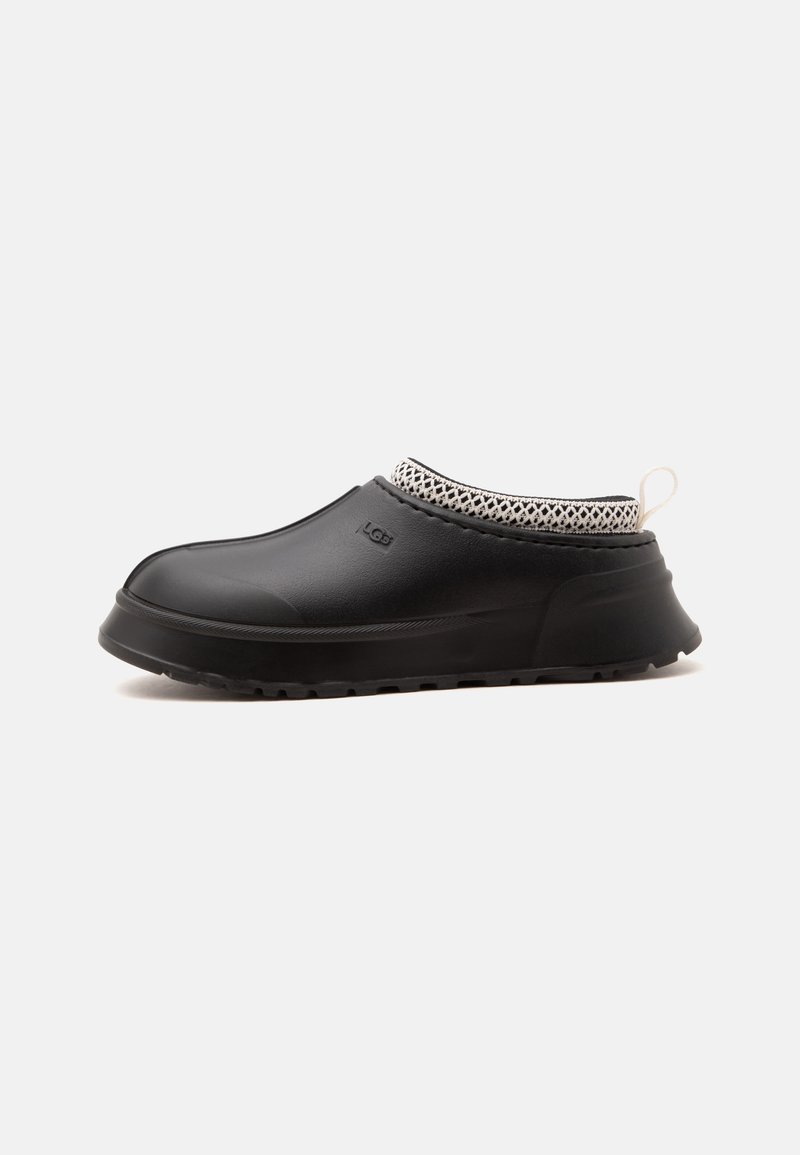 Chaussure noire sans lacets avec col tricoté texturé, semelle en caoutchouc et languette au talon, vue latérale sur fond blanc.