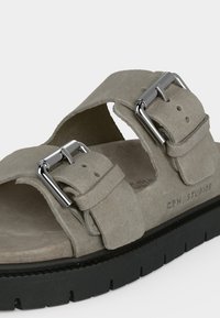 Sandale en daim beige avec deux boucles argentées réglables et semelle noire rainurée, marquée "CPH Studios" sur le côté.