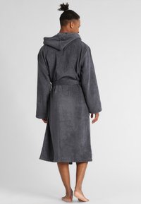 Szary, kapturowy szlafrok wykonany z miękkiej, teksturowej tkaniny, z długimi rękawami, paskiem do zawiązywania oraz długością do kolan.